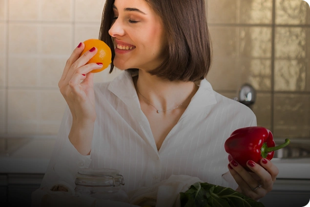 Woman smiling while holding an orange and red pepper