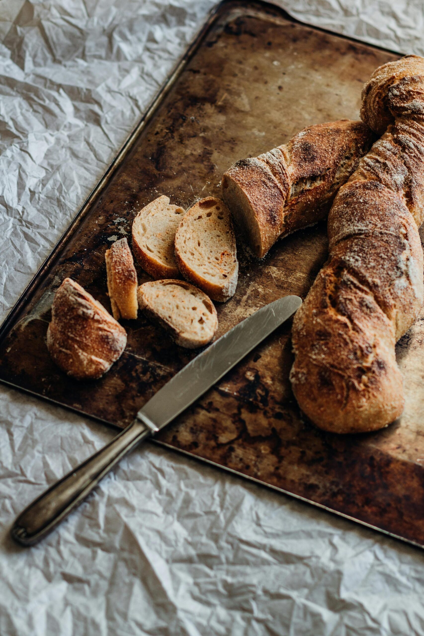 Sliced whole-grain bread on a baking tray with a knife